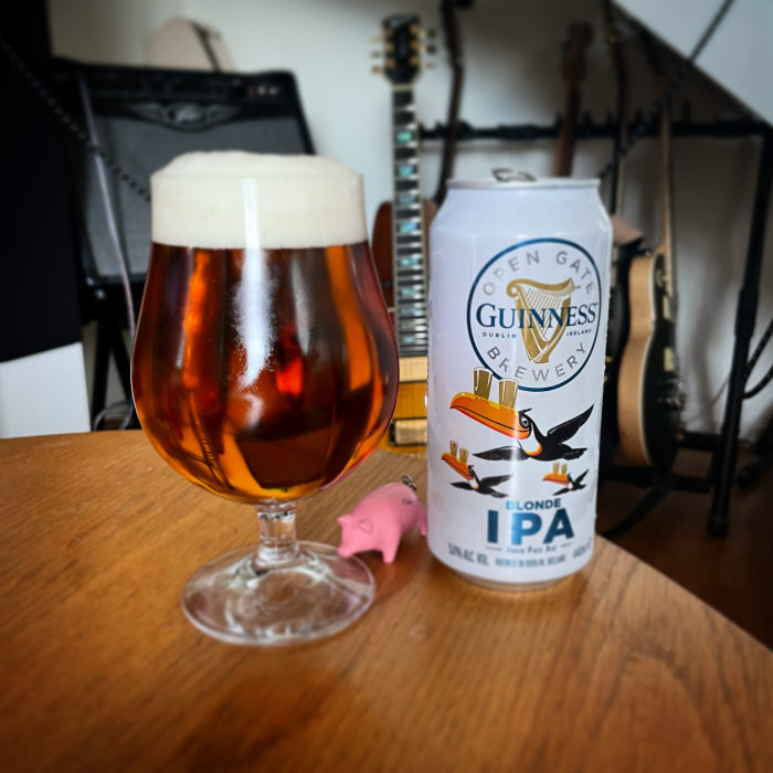 Ett glas med öl bredvid en burk av Guinness Blonde IPA på ett bord med en gitarr i bakgrunden.