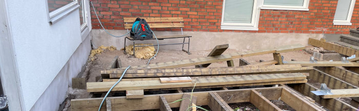 En före och efter bild av en husvägg där putsrenovering pågår, med byggbrädor i förgrunden.