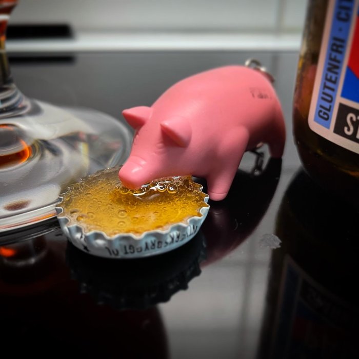 En rosa spargris vid ett öllock fyllt med bärnstensfärgad vätska, bredvid en ölflaska.