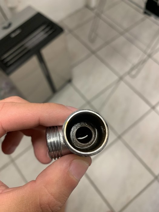 Hand håller en metallisk rördel med gängning och synlig inre smuts.