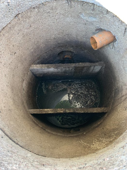 Bild av en öppen avloppsbrunn med synligt avloppsrör och vattenansamling.