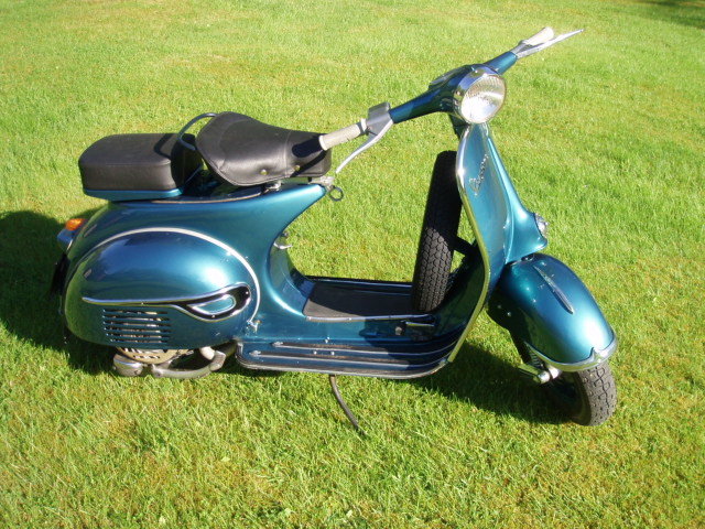 Blå Vespa scooter från 1959 parkerad på gräsmatta i solljus.