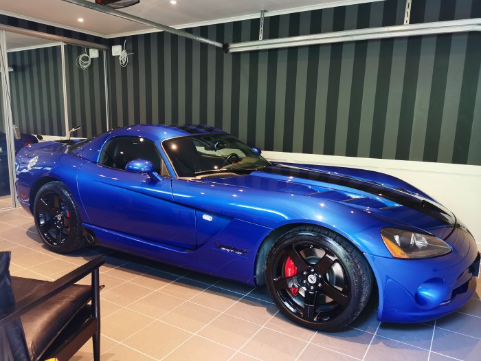 Blå sportbil parkerad inomhus, troligtvis en Dodge Viper, med svarta detaljer och fälgar.