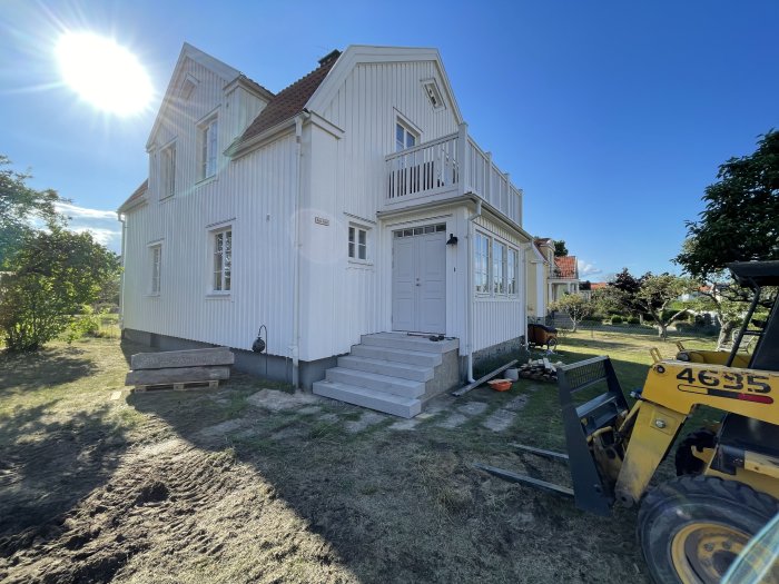 Nybyggd stentrappa framför husets huvudentré med en minilastare till höger och granitblock på gräsmatta.