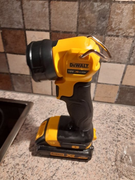 Gul och svart batteridriven skruvdragare av märket DeWALT på ett köksbord, bakgrund av kakel.