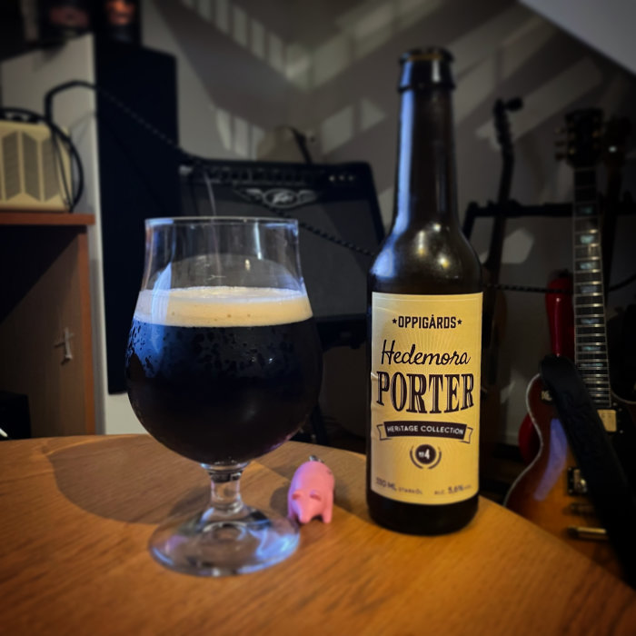 Flaska och glas av Hedemora Porter på ett bord med en gitarr och förstärkare i bakgrunden.