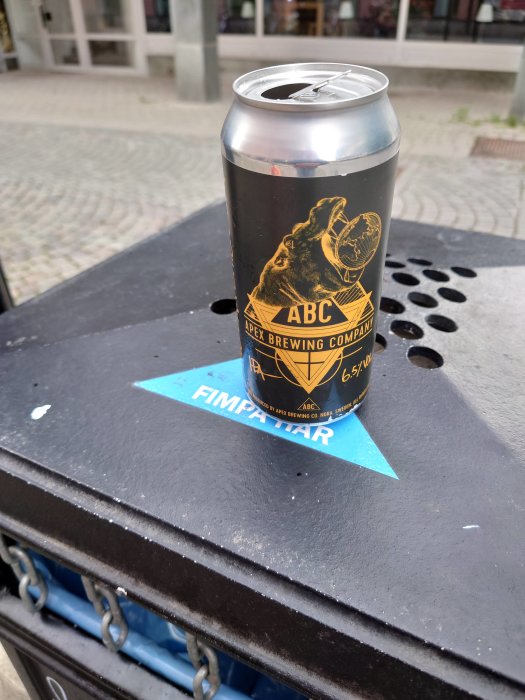 Öppnad ölburk från Apex Brewing på en papperskorg med texten "Fimpa Här".