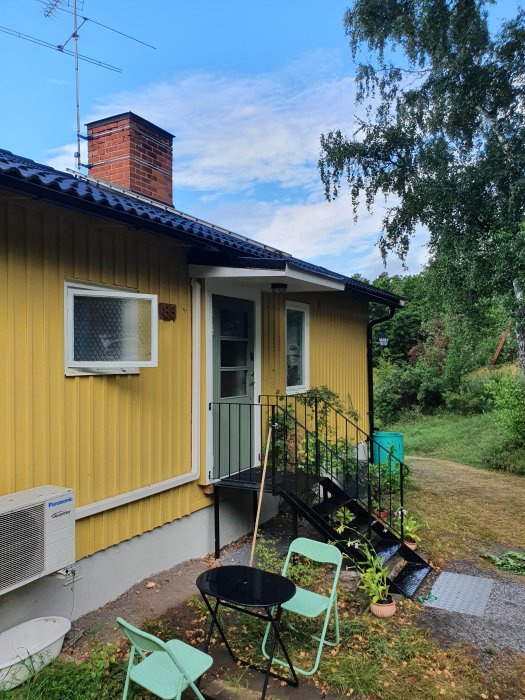 Gult hus med nybyggd ram och tak av plywood ovanför entré samt hemmagjord vindskiveplåt på takkanten.