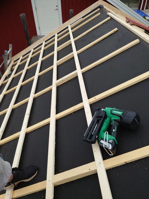 Takstolar under konstruktion på ett hus med spikpistol och personens sko i förgrunden.