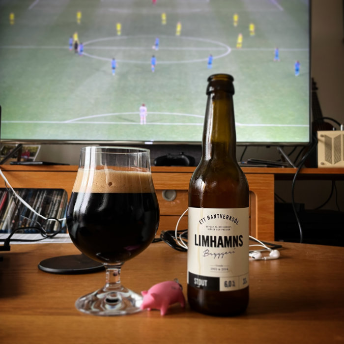 Öppnad ölflaska och glas framför en fotbollsmatch på TV-skärmen.