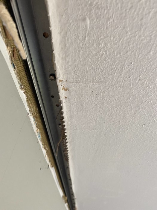 Metallister längs väggens övre kant med exponerad uppspänd papp och borttagna skugglister i ett vardagsrum under renovering.