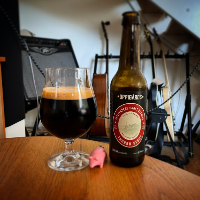 Flaska Öppigårds öl och ölglas på bord framför musikinstrument.