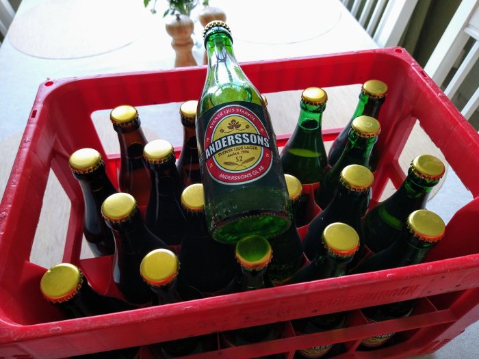 En back med 33 cl gröna returglasflaskor av Anderssons Lager 5.2% på ett vitt bord.