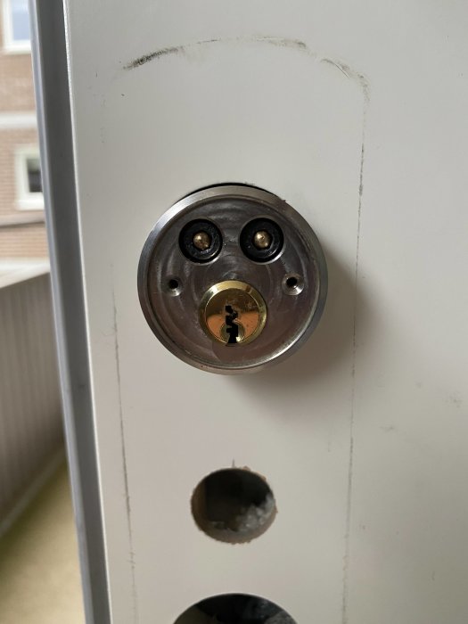 Närbild av en låscylinder i en dörr, slitage syns runtomkring låset.