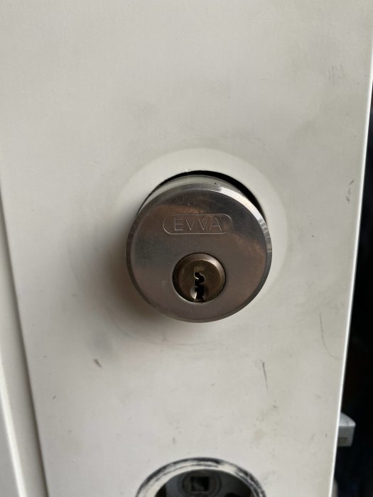 EVVA låscylinder i en vit dörr, söker råd för byte till ASSA-cylinder.