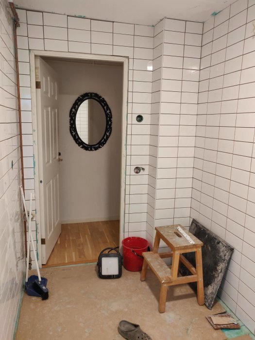 Nyligen kaklat badrum med vita väggplattor, verktyg och arbetsmaterial synliga, listar ej slutförda.