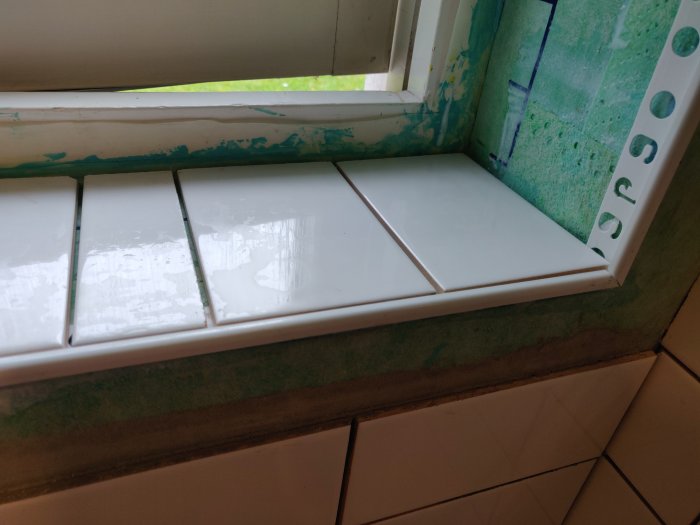 Nylagda vita kakelplattor runt ett fönster i ett badrum under renovering.
