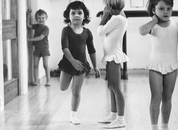 Svartvit bild av barn i gymnastikkläder, en dansar, två pratar, 80-talets stil.