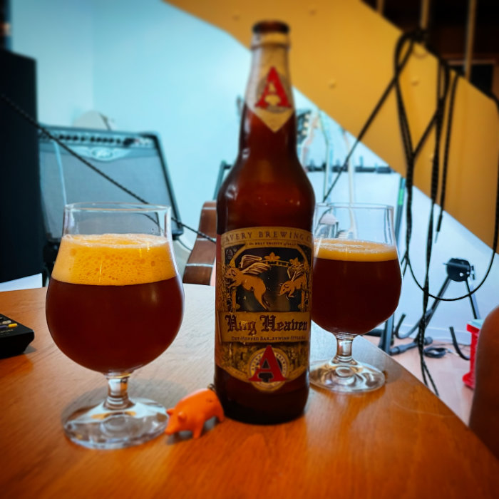 En ölflaska och två glas fyllda med mörk öl på ett bord, med musikutrustning i bakgrunden.