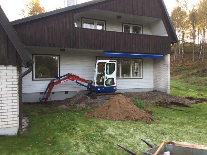 Hus med pågående fasadbyte och en minigrävare framför gavelbalkongen som söker renoveringstips.