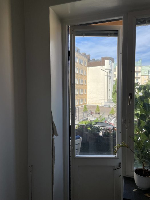 Skadade putsade fönstersmygar med krullande pappersmaterial i en 30-talslägenhet, med utsikt över stadsmiljö.