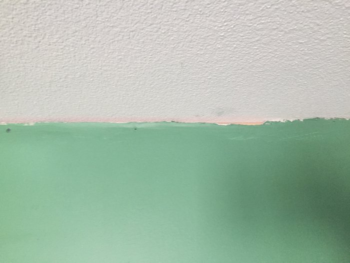 Väggmöte med glipa där träreglar syns under taket i ett ofärdigt sovrum.