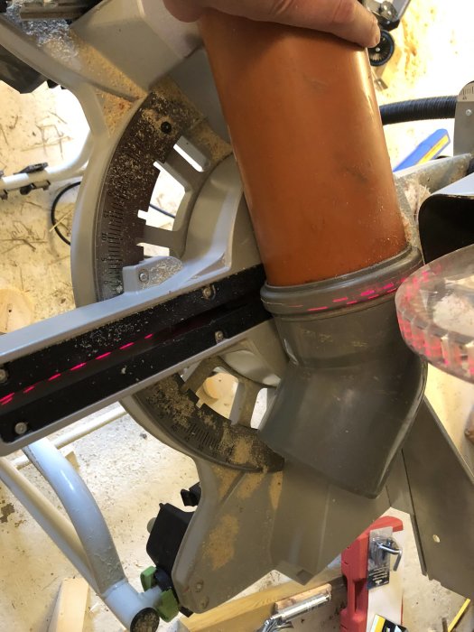Hand som håller en plastavloppsrör bit ovanför en geringssåg i en verkstad, indikerar DIY-projektarbete.