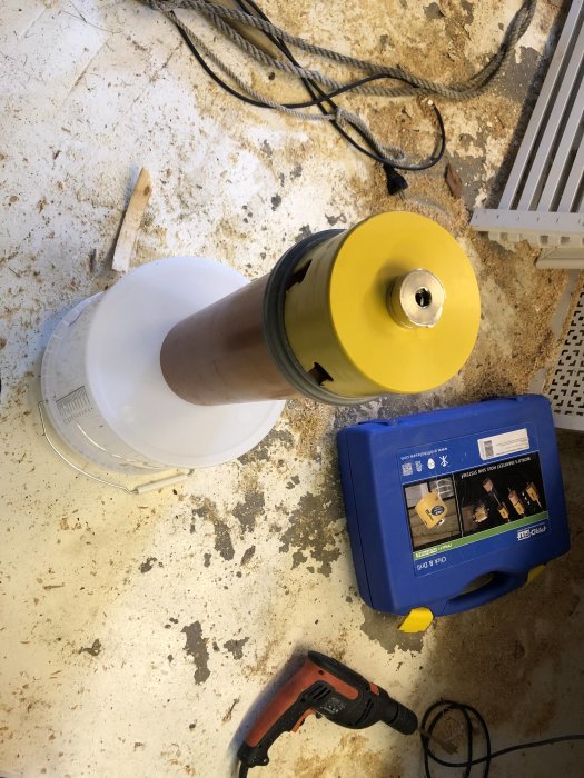 Översiktsbild på ett DIY-projekt med en vit hink som har flera hål borrade i sig, verktyg och byggmaterial syns runtomkring.