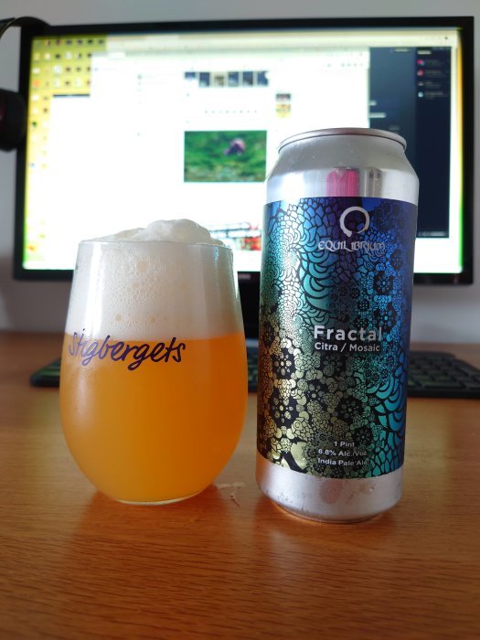Ett glas öl med skum och en burk IPA på ett skrivbord framför en datorskärm som visar ett forum.