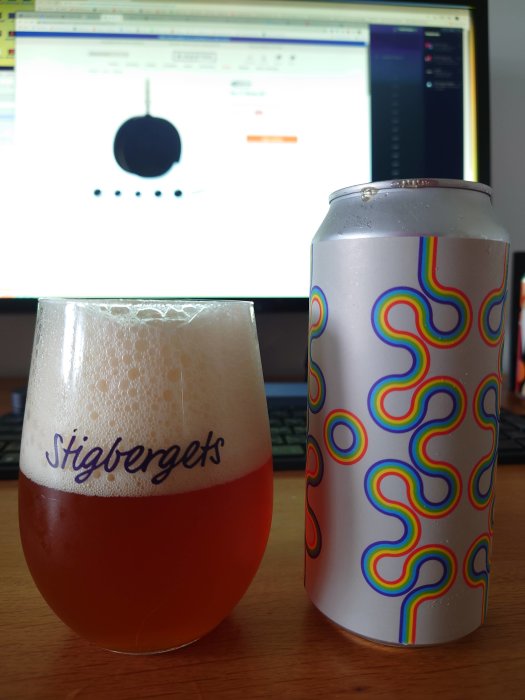 Ölglas märkt "Stigbergets" och färgglad ölburk framför en datorskärm, inomhusmiljö.