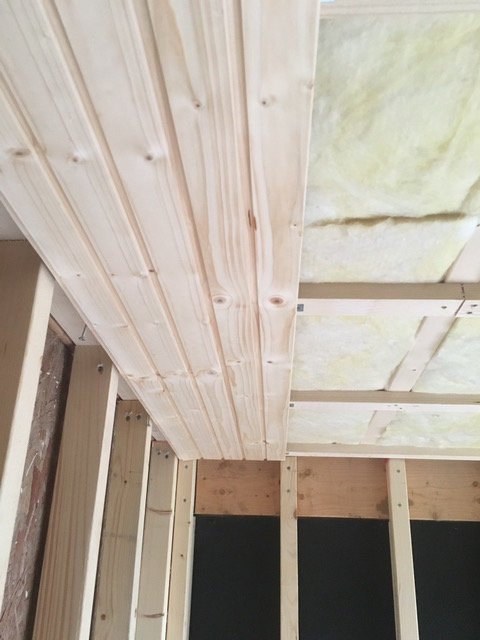 Nyinstallerade takpaneler av trä och synlig isolering mellan takbjälkar under renovering.