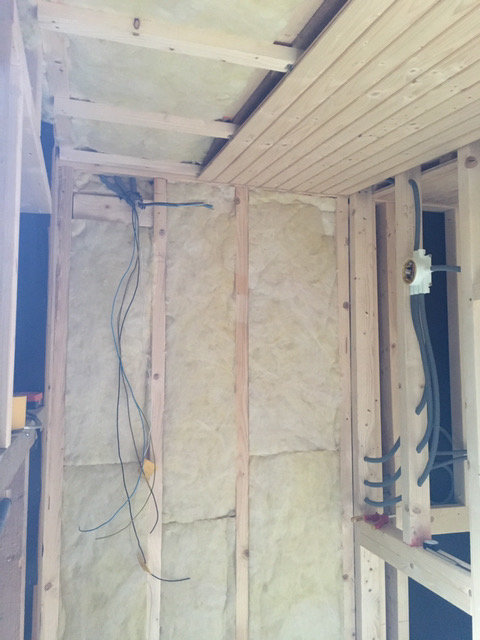 Isolerad väggsektion under konstruktion med elledningar och träreglar.