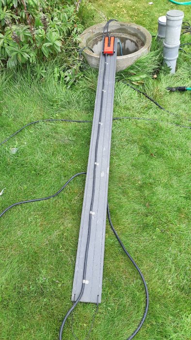 Composite decking with a drainage pump level sensor attached, placed over a lawn near a well opening.
