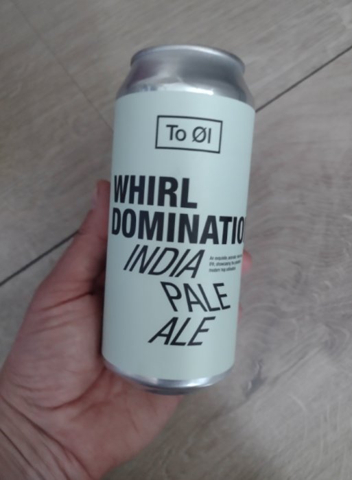Burk av To Øl Whirl Domination India Pale Ale hållen i en hand mot ett trägolv.