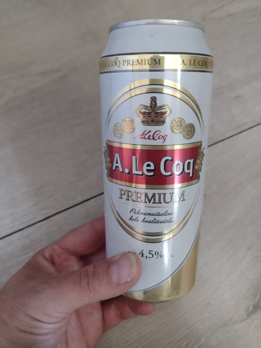 Hand håller en A. Le Coq Premium ölburk med estnisk text och alkoholhalten 4,5 % synlig.