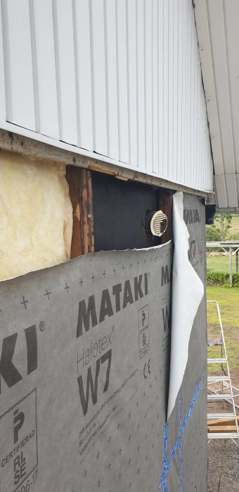 Väggparti under isolering med synligt utlopp för köksfläkt och isolermaterial.