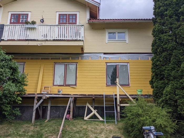 Nyinstallerad träpanel ovanför fönster på gult hus, byggställning och verktyg syns.