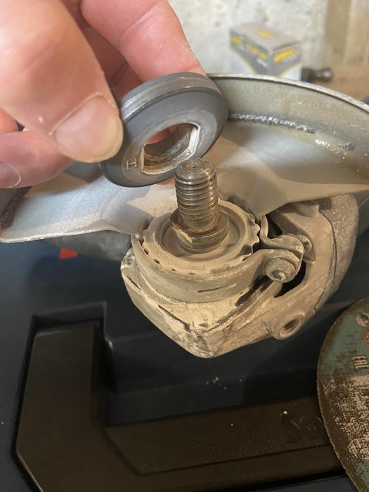 Hand håller en övre låsring nära en slipmaskins axel redo för montering av slip- eller kapskiva.