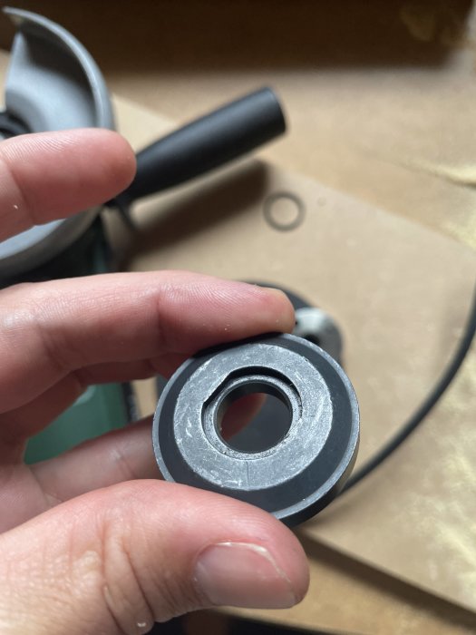 Metallskiva med ojämn yta hålls mellan fingrarna, möjlig skada synlig.