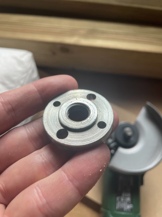 Metallbricka hålls i handen framför en suddig bakgrund av verktyg och trämaterial.