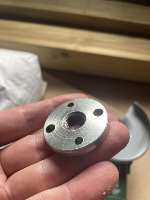 Närbild av en hand som håller ett metallstycke med hål, troligen en byggnadskomponent.