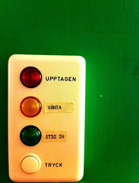 Signalpanel med röd, gul och grön lampa märkta "UPPTAGEN", "VÄNTA" och "STIG IN" på en grön vägg.