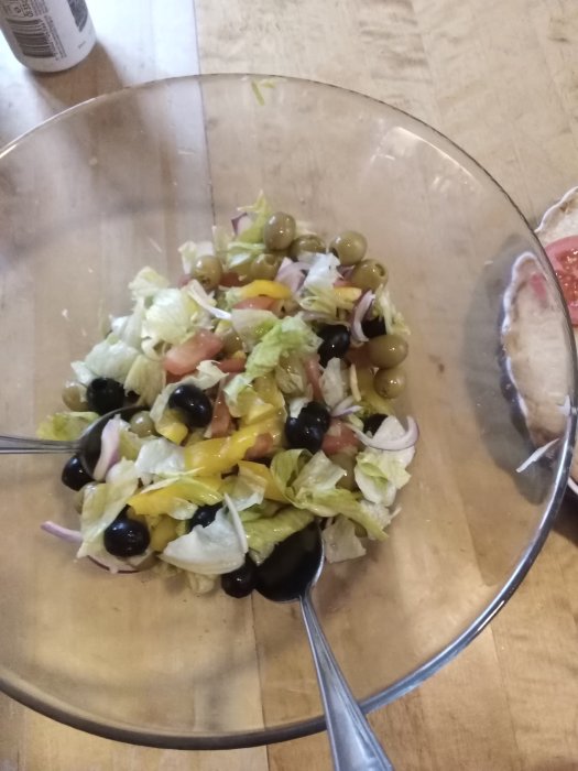 Sallad med oliver och rödlök i en genomskinlig skål på ett träbord.