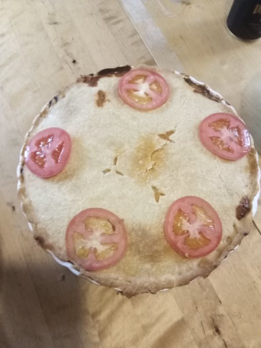 Hemgjord tacopaj med tomat på toppen på ett träbord.