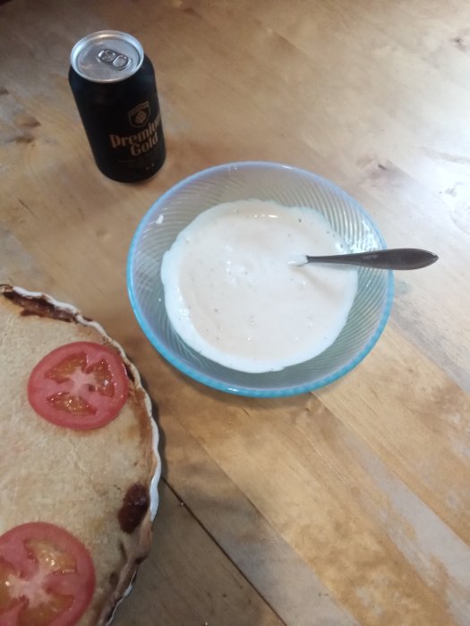 Hembakad tacopaj med skivad tomat, skål med vitlökssås och en burk öl på ett träbord.