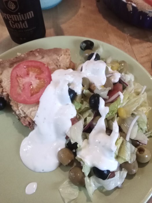 Tallrik med tacopaj, sallad med oliver och rödlök, toppad med vitlökssås och grön tabasco.