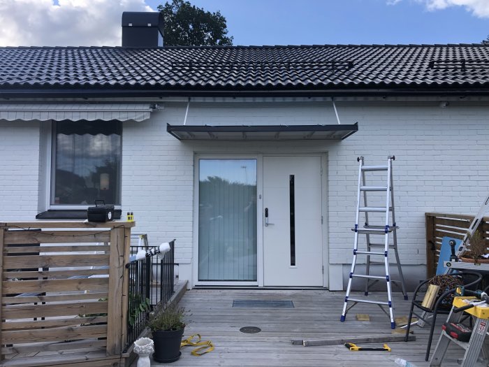 Entrétak installerat över en vit dörr på hus med ställning och byggmaterial framför.