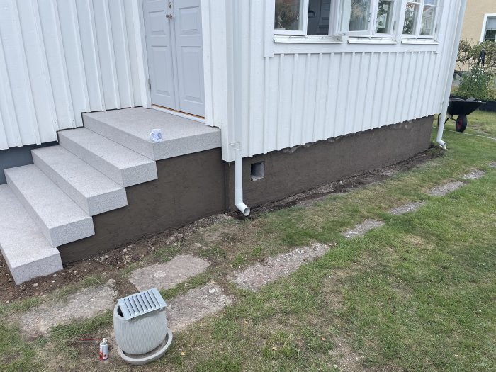 Nyinstallerade betongtrappsteg vid husentré med nypålagd puts på fundamentet och oputsad verandagrund.