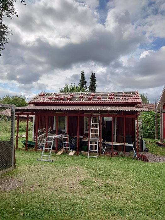 Ett rött hus under takrenovering med betongpannor och stegar som används för installation.