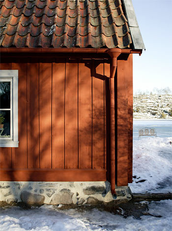 Vägg på ett hus med röd matt färg i vinterlandskap, perfekt för diskussion om målningsprojekt utomhus.